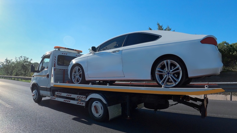 A Tow truck carrying a white car on a highway flatbed in Greenville, SC