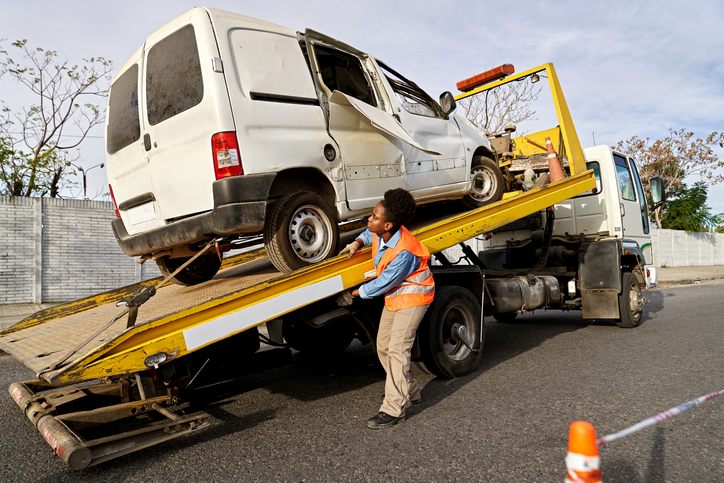 Worker loading damaged van onto a flatbed tow truck in Greenville, SC